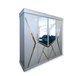 Modern white almirah with geometric gold accents and mirrored doors, placed in a cozy bedroom with wooden furniture and decor.