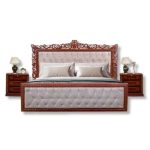 Luxury wooden king-size bed with elegant carved headboard, tufted upholstery, and matching bedside tables in a classic bedroom interior.