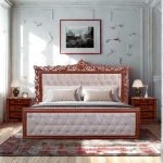 Luxury wooden king-size bed with elegant carved headboard, tufted upholstery, and matching bedside tables in a classic bedroom interior.