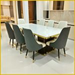 Modern marble top dining table with eight upholstered chairs in gray and white, featuring quilted design and gold accents, perfect for a luxury dining room.