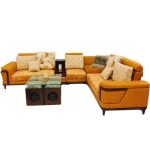 Modern L-shaped sectional corner sofa in mustard yellow fabric with printed and plain cushions, paired with glass-top wooden center tables.