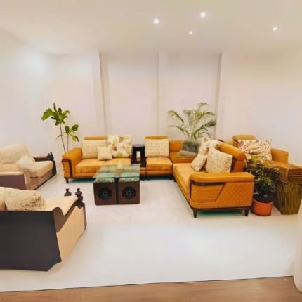Modern L-shaped sectional corner sofa in mustard yellow fabric with printed and plain cushions, paired with glass-top wooden center tables.