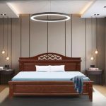 A bedroom featuring a large, dark wooden bed with an ornate, carved headboard. The bed has a light blue mattress and a dark blue blanket draped over the foot of the bed. On either side are modern, round nightstands with small pendant lights hanging above them. A large, circular light fixture hangs from the ceiling in the center of the room. The walls are a mix of light wood paneling and textured wallpaper.
