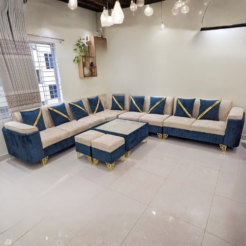 Sectional Corner Sofa Luxurious L-shaped sectional sofa in blue and beige velvet upholstery, featuring gold metal legs and matching ottomans, set in a modern living room with bright lighting and elegant décor.