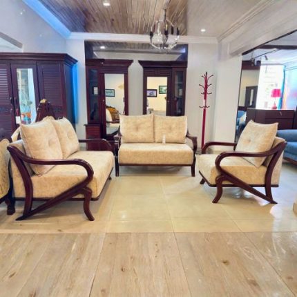 A classic wooden-frame sofa set with cream upholstered cushions arranged in a showroom, featuring a 3-seater, 2-seater, and single chair, displayed against wooden cabinets and bright lighting.